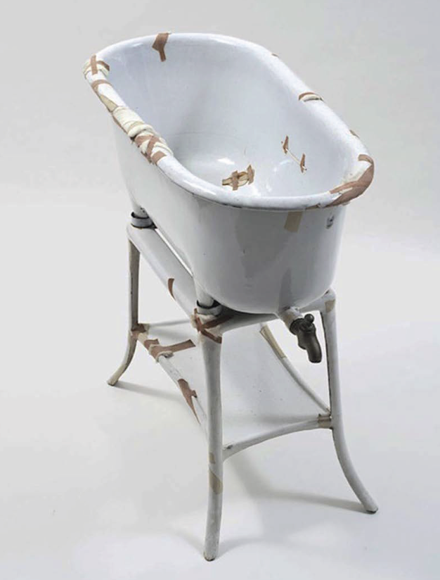 Alte weiße Emaille-Badewanne auf Metallgestell, abgeplatzter Lack, kleiner Wasserhahn.